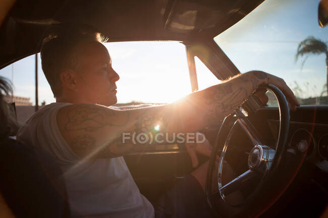 Homme conduite voiture vintage au coucher du soleil — Photo de stock