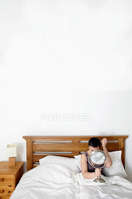 Frau im Bett, Blick in den Spiegel — Stockfoto