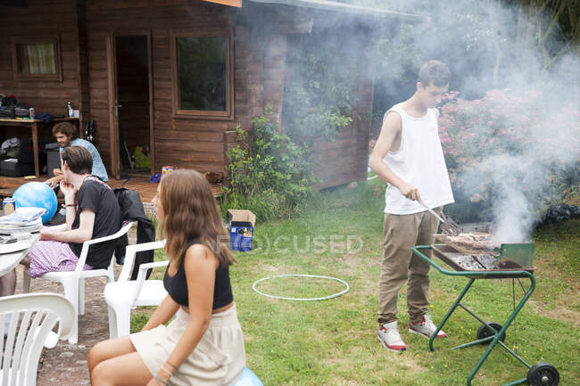 Quatro jovens amigos adultos no jardim fazendo churrasco — Fotografia de Stock