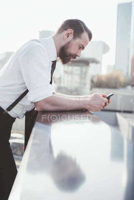 Stylish businessman reading smartphone text leaning against office balcony — Stock Photo