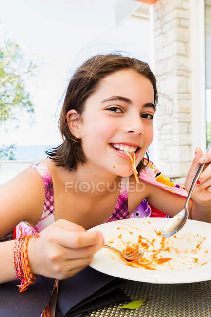 Улыбающаяся девушка ест пасту на открытом воздухе — стоковое фото