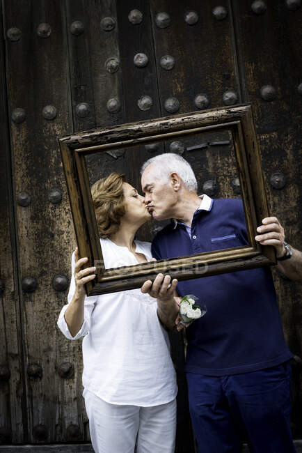 Portrait of senior couple, kissing, holding wooden frame in front of their faces, Mexico City, Mexico — Stock Photo