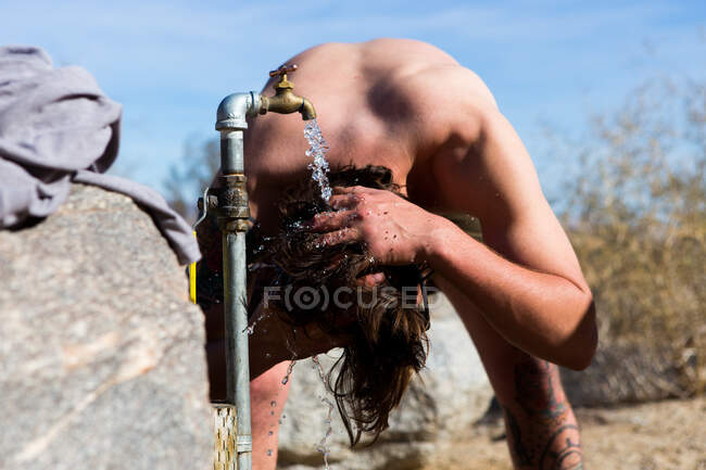 Giovanotto che lava i capelli sotto il rubinetto del campeggio, Anza-Borrego Desert State Park, California, USA — Foto stock