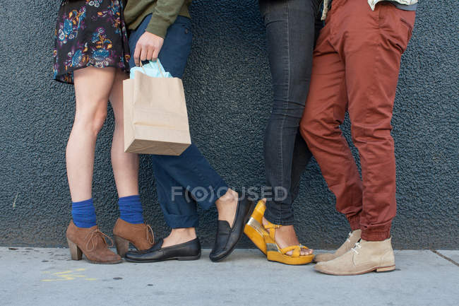 Four young adults standing by wall, low section — Stock Photo