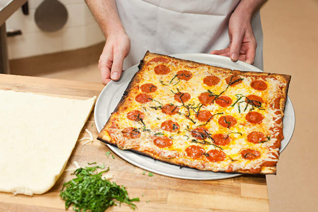 Обрезанный вид на мужского шеф-повара, держащего поднос с пиццей — стоковое фото