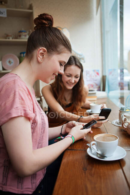 Mujeres jóvenes en la cafetería usando teléfonos celulares - foto de stock