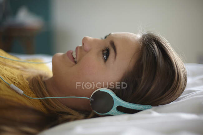 Portrait of teenage girl lying on bed listening to headphones — Stock Photo