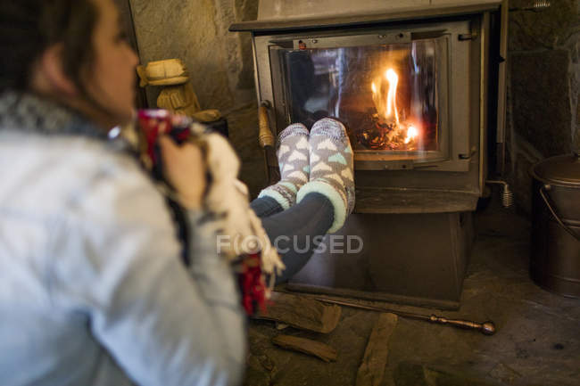 Young woman warming feet in front of fire — Stock Photo