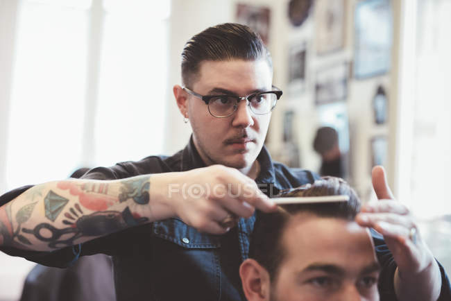 Barbiere pettinare i capelli del cliente nel negozio di barbiere — Foto stock