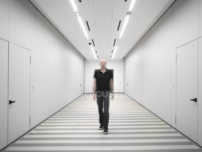 Hombre vistiendo ropa negra caminando por corredor blanco - foto de stock