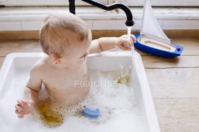 Bebê menino tomando banho na pia da cozinha tocando água corrente — Fotografia de Stock