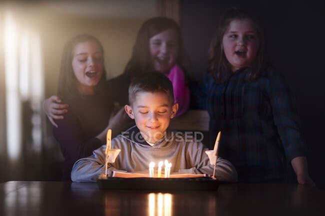 Хлопчик, оточений друзями, дивлячись на день народження торт посміхається — стокове фото