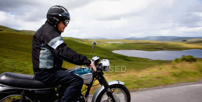 Senior masculino andar de moto através da paisagem rural — Fotografia de Stock