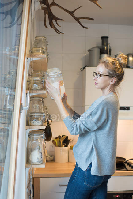 Frau liest Etikett auf Glas in Küche — Stockfoto