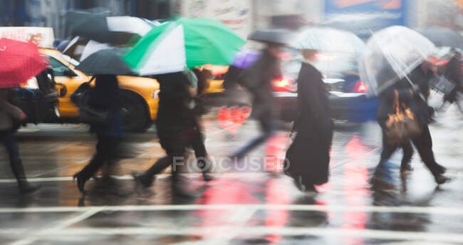 Ligne de personnes traversant la rue de la ville sous la pluie — Photo de stock