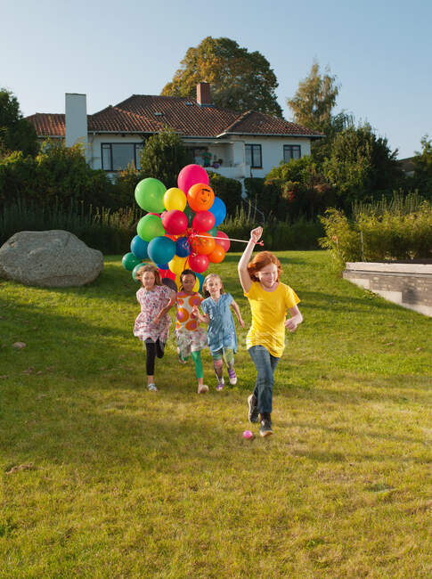 Девушки бегают по газону с разноцветными воздушными шарами — стоковое фото