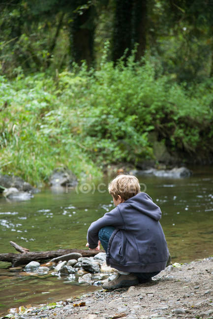 Rapaz agachado e a olhar para o riacho — Fotografia de Stock