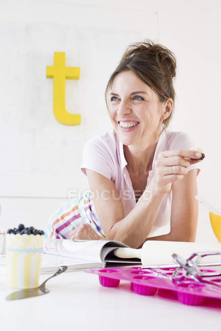 Mujer madura descansando en el codo sosteniendo el producto horneado mirando hacia otro lado sonriendo - foto de stock