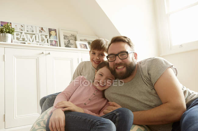 Portrait d'un homme mi-adulte avec son fils et sa fille allongés sur une chaise de sac à haricots — Photo de stock
