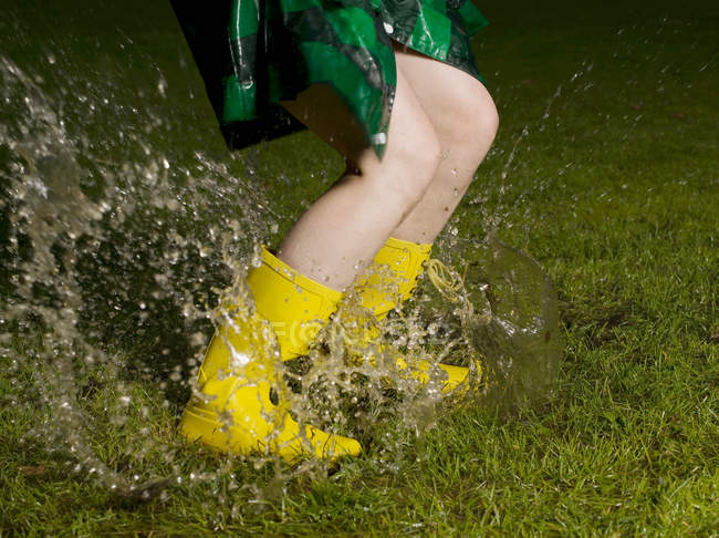 Woman wearing rubber boots jumping in rain puddle — Stock Photo