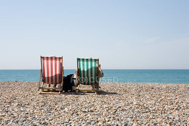 Rear view of deople in deckchairs at sandy beach — Stock Photo