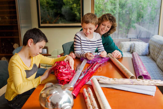 Woman and sons wrapping gifts at table — Stock Photo