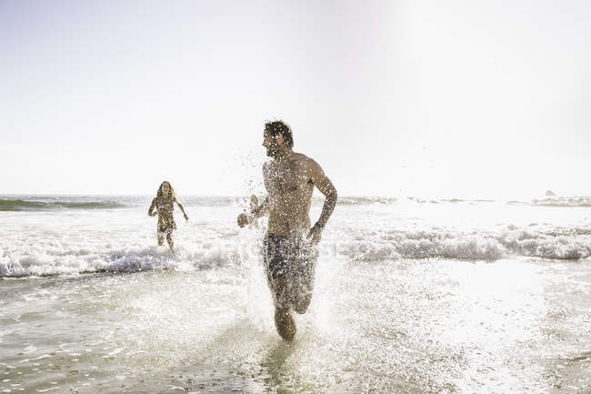 Mid adult couple wearing swimming shorts running in sea, Cape Town, South Africa — Stock Photo