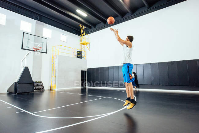 Male basketball player jumping to throw ball in basketball hoop — Stock Photo