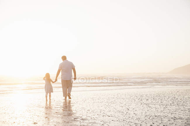 Father and daughter holding hands paddling in ocean — Stock Photo