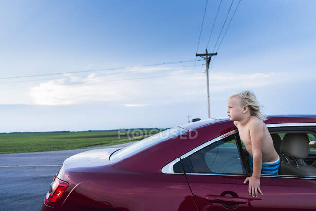 Menino inclinado para fora da janela do carro olhando para longe — Fotografia de Stock