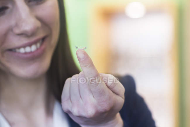 Жінка тримає контактну лінзу на пальці посміхаючись — стокове фото