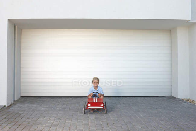 Jeune garçon assis dans une voiture jouet — Photo de stock