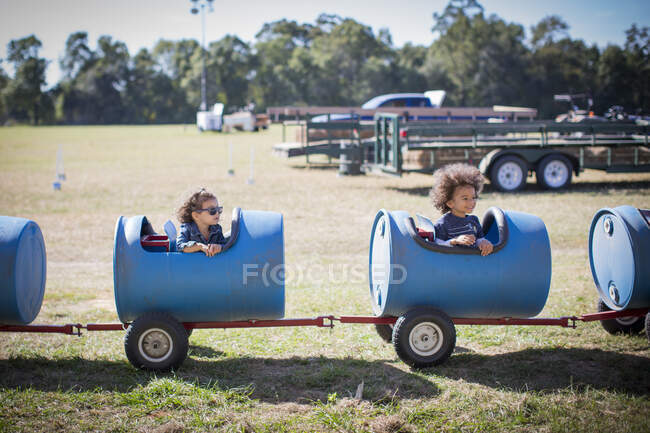 Niños sentados en el carro del barril mirando hacia otro lado sonriendo - foto de stock