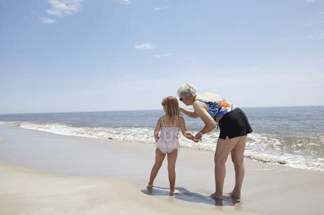 Mujer mayor señalando a su nieta en la playa - foto de stock