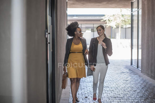 Dos jóvenes empresarias caminando y hablando fuera de la oficina - foto de stock