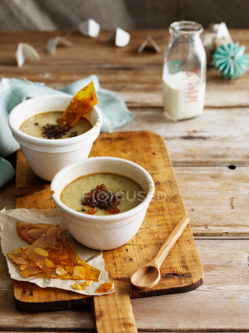 Bowls of custard with nut brittle and wooden spon — Stock Photo