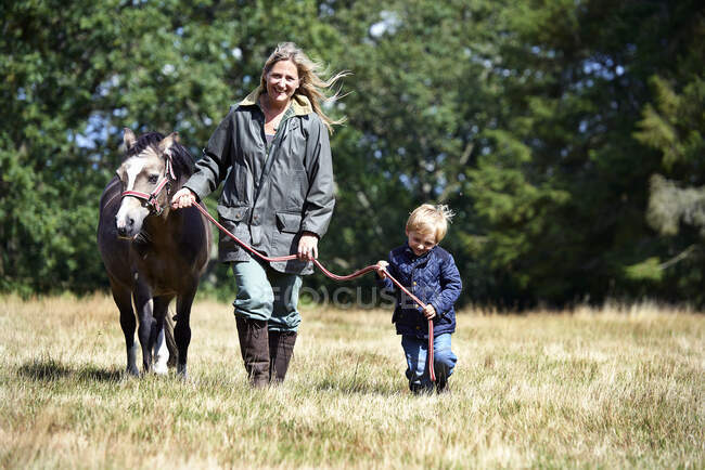 Madre e hijo caminando pony en el campo - foto de stock