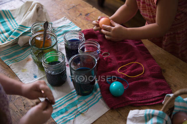 Руки двох молодих сестер фарбують пасхальні яйця в глеках за столом. — стокове фото