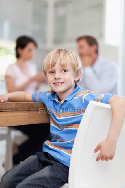 Усміхнений хлопчик сидить за столом, фокус на передньому плані — стокове фото