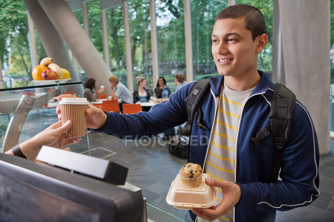 Estudiante universitario pagando en cafetería universitaria - foto de stock