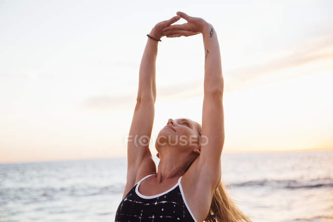 Женщина на пляже подняла руки, делая упражнения на растяжку — стоковое фото