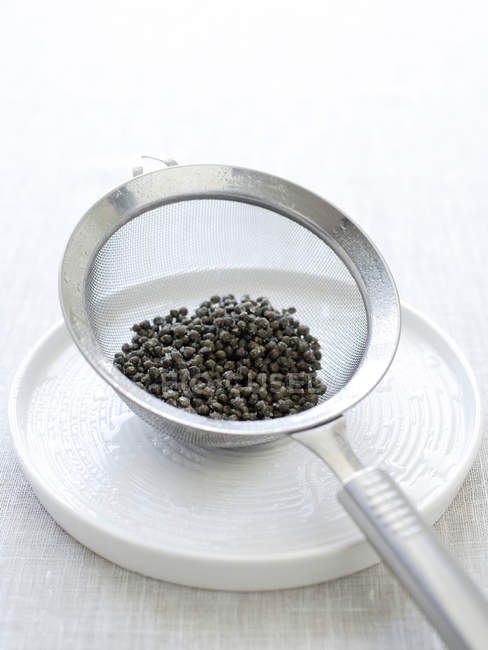 Baby capers in sieve on plate — Stock Photo