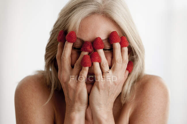 Mature woman wearing raspberries on fingers and covering face — Stock Photo
