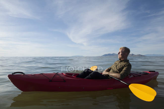 Vista lateral del joven en kayak en agua sosteniendo paletas, ojos cerrados, Great Salt Lake, Utah, EE.UU. - foto de stock
