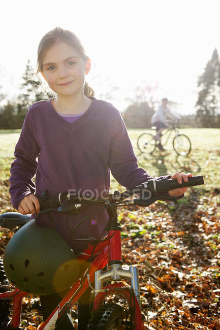 Девушка ходит на велосипеде по лугу, мальчик на заднем плане — стоковое фото