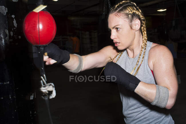 Boxeadora femenina perforando una bola de boxeo en el gimnasio - foto de stock