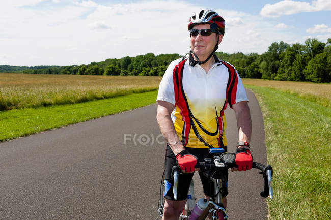 Senior man riding bicycle through countryside — Stock Photo