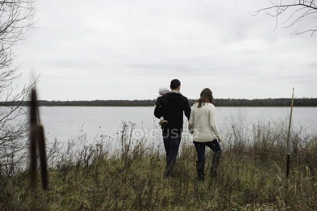 Молодая семья прогуливается на свежем воздухе, рядом с озером, вид сзади — стоковое фото
