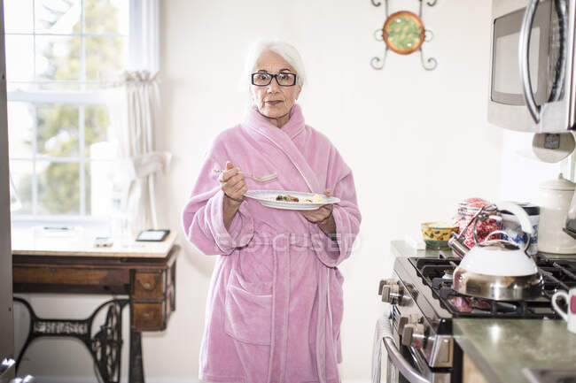 Retrato de mulher idosa em casa em pé e comer em seu manto em seu kiche — Fotografia de Stock