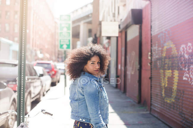 Jovem mulher andando rua abaixo olhando sobre o ombro — Fotografia de Stock
